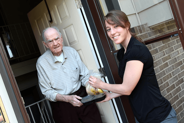 A Meals on Wheels volunteer delivering a meal to a senior